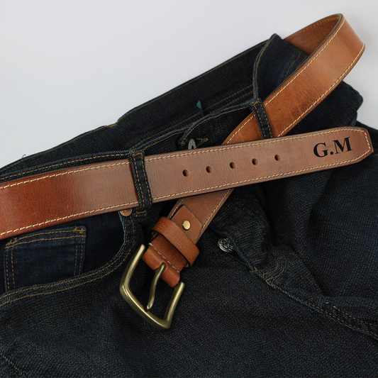 Brown leather belt with brass buckle on a dark fabric background