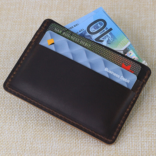 Dark brown handmade leather card holder wallet featuring a minimalist slim design with two credit cards and Australian ten-dollar bills tucked inside.