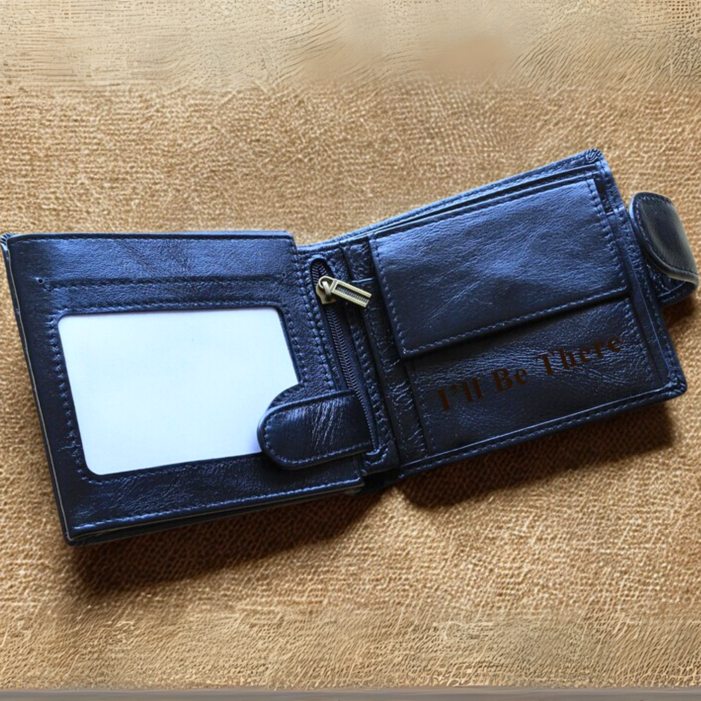 Black leather trifold wallet with 'I'll Be There' engraving on a beige textured surface