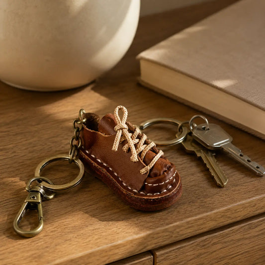 Brown leather shoe keychain displayed with keys and brass hardware on a wooden table