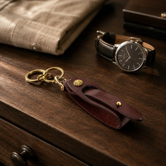 Brown leather key holder with brass hardware styled beside wristwatch and accessories on a wooden table