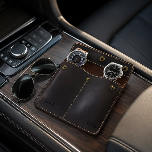 Vintage dark brown leather double watch pouch displayed on a luxury car center console beside black sunglasses with soft daylight and premium masculine interior details.