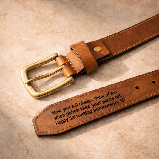 Personalized brown genuine leather belt with gold-tone buckle and engraved romantic anniversary message on the inner strap, displayed on a neutral stone background with premium handcrafted detail.
