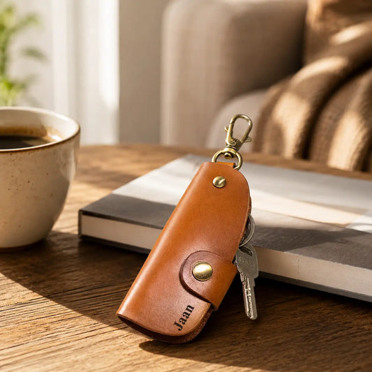 Personalised tan leather key holder with attached keys displayed beside coffee and books on a wooden table