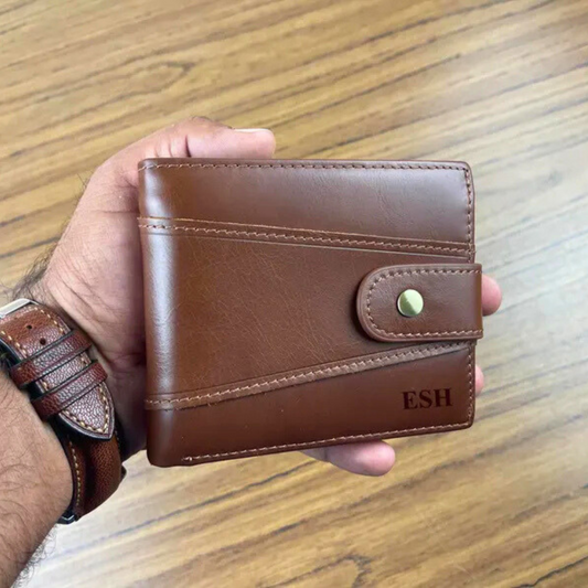 Personalised brown leather wallet with 'ESH' initials engraved on it, held by a hand on a wooden surface