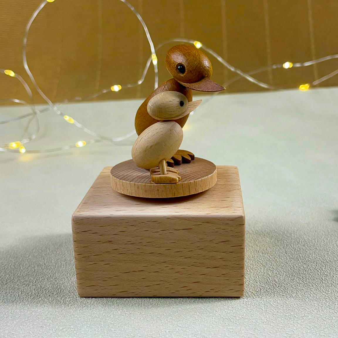 A wooden duck and duckling figurine mounted on a rectangular wooden block, used as a decorative ornament.