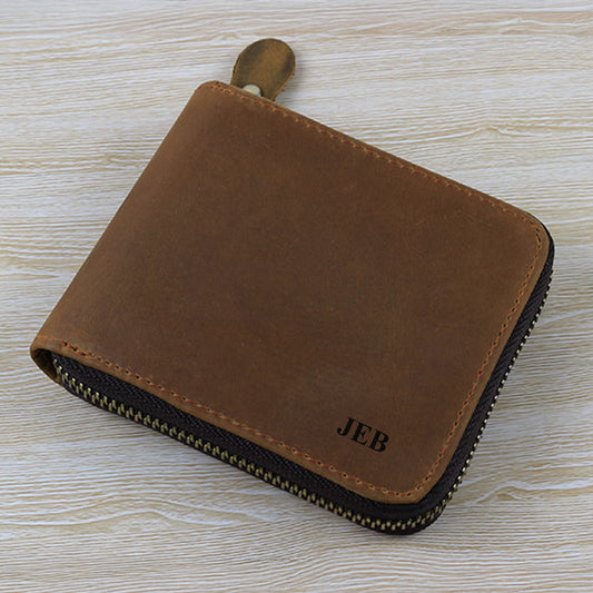 Brown leather zipper wallet with 'JEB' engraving on a light wood surface