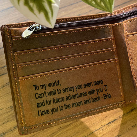 Brown leather wallet with engraved message on a wooden surface