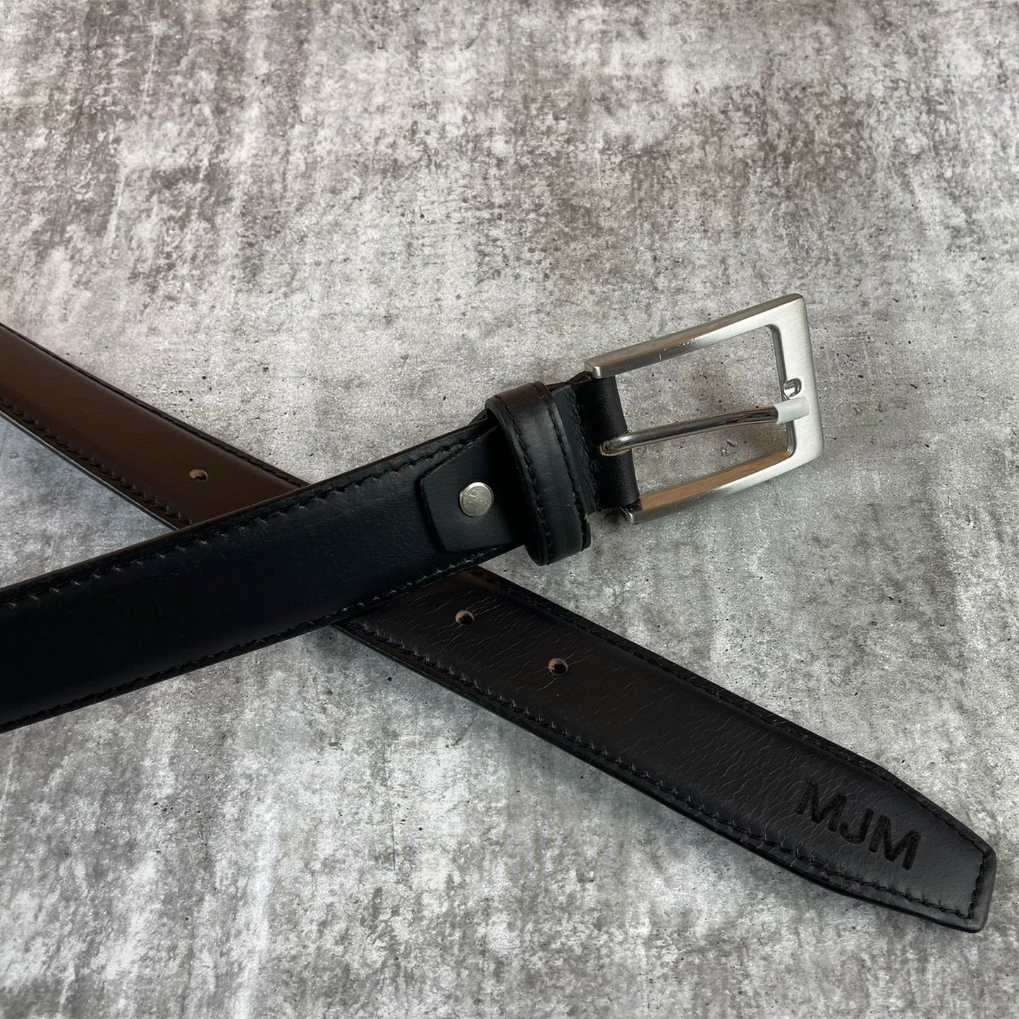 Black leather belt with silver buckle on a gray textured surface