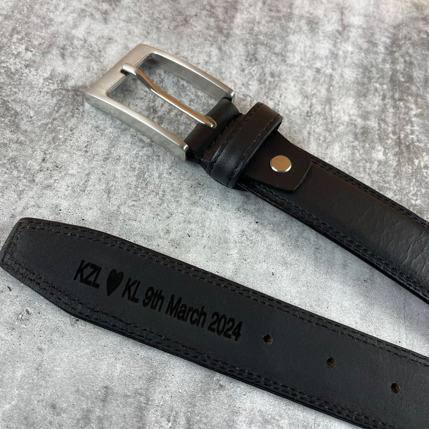 Black leather belt with engraved text on a gray surface