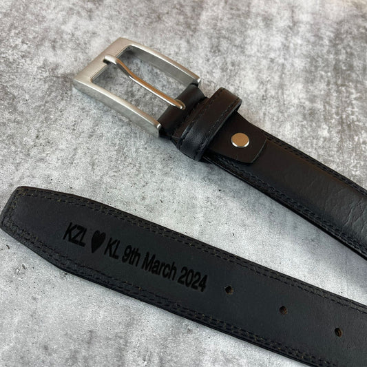Black leather belt with engraved text on a gray surface