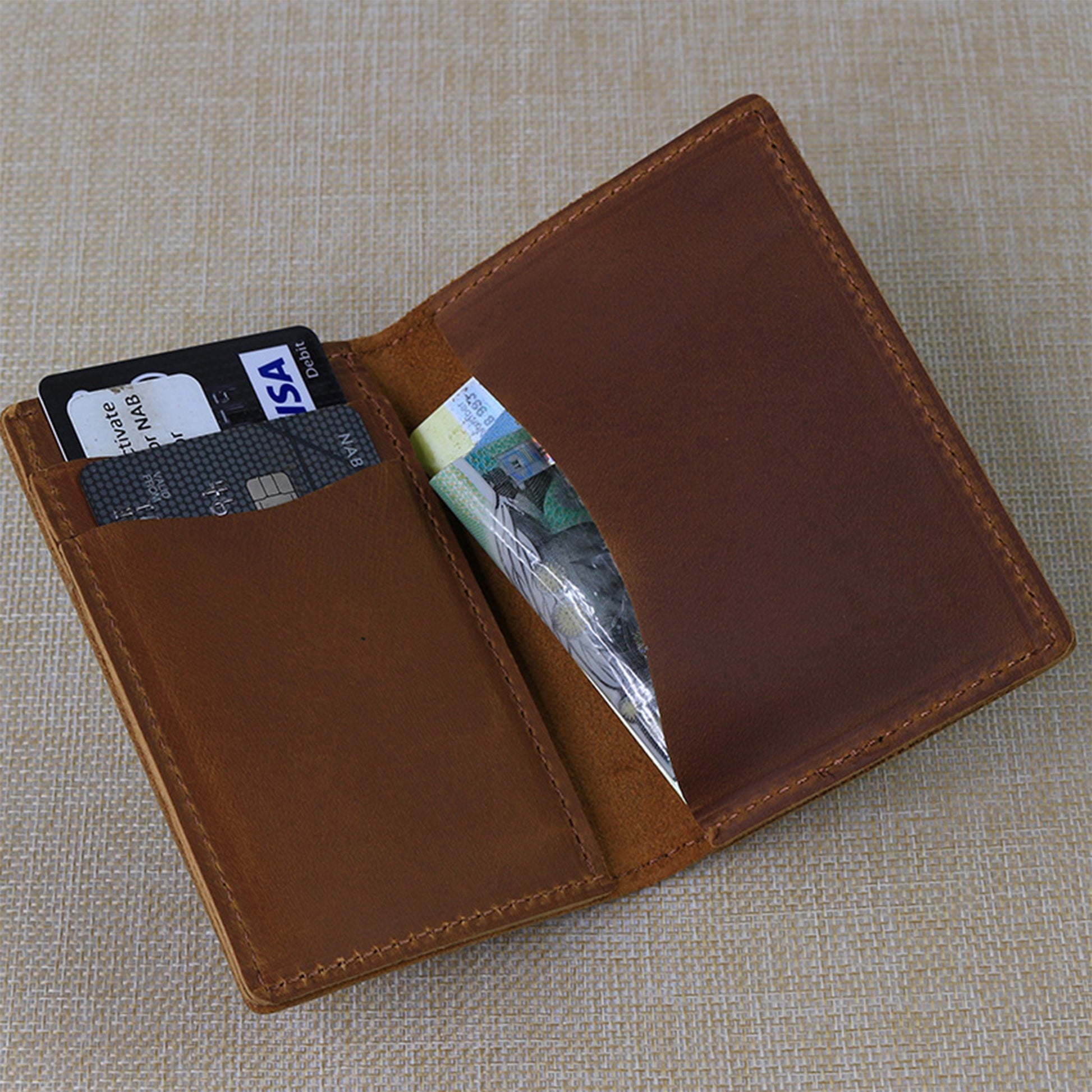 Custom engraved men's leather wallet interior displaying personalized text, bank cards, and cash, highlighting the compact bifold design.