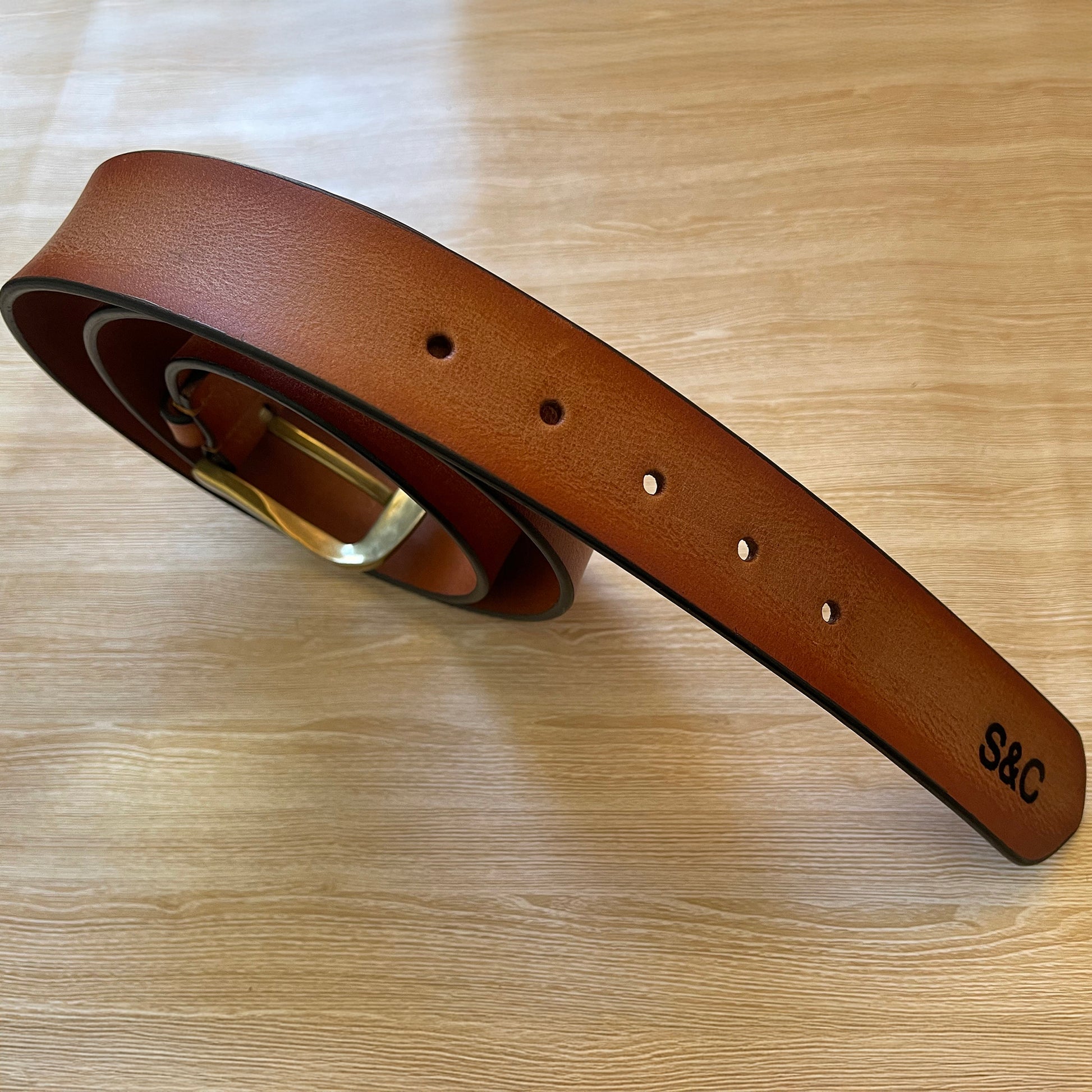 Brown leather belt with brass buckle on a wooden surface