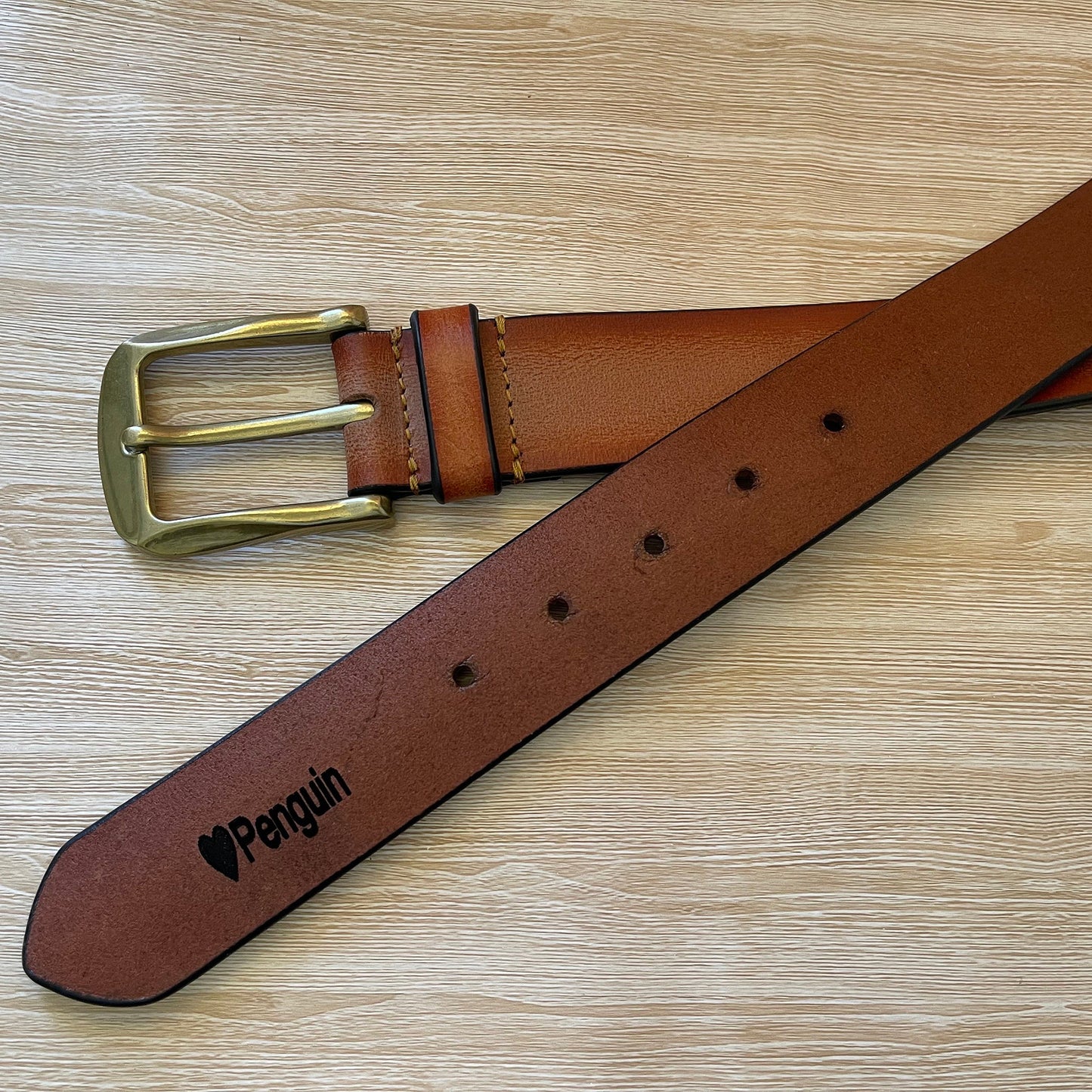 Brown leather belt with brass buckle on a wooden surface