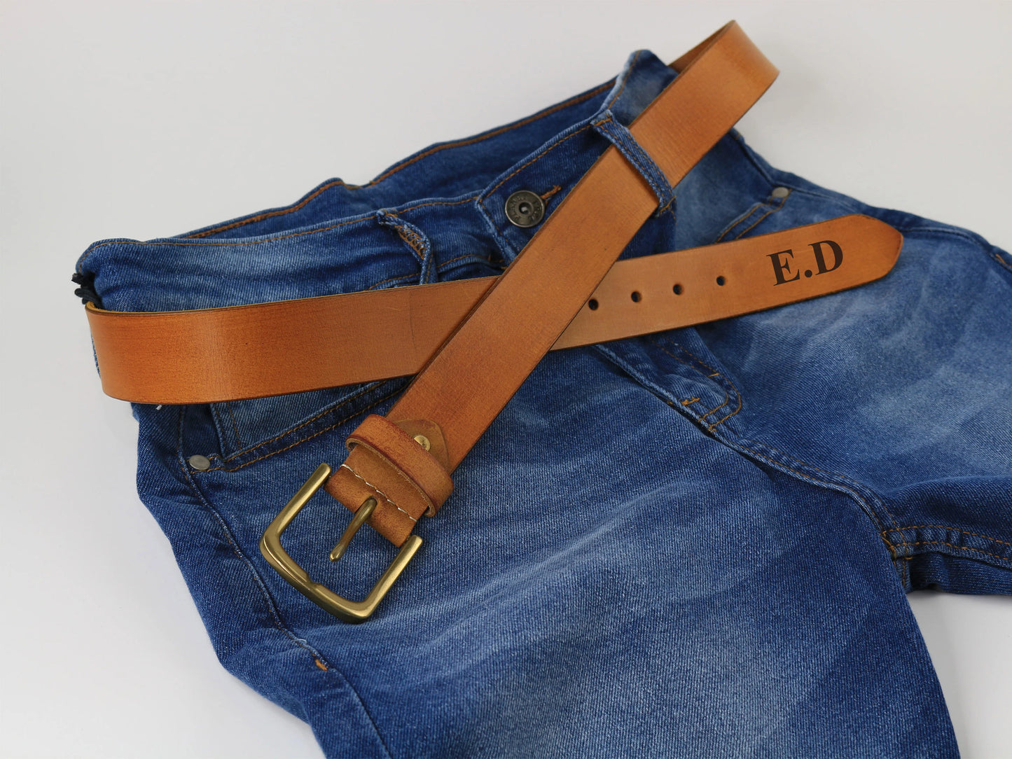 Blue jeans with a brown leather belt featuring initials on a white background