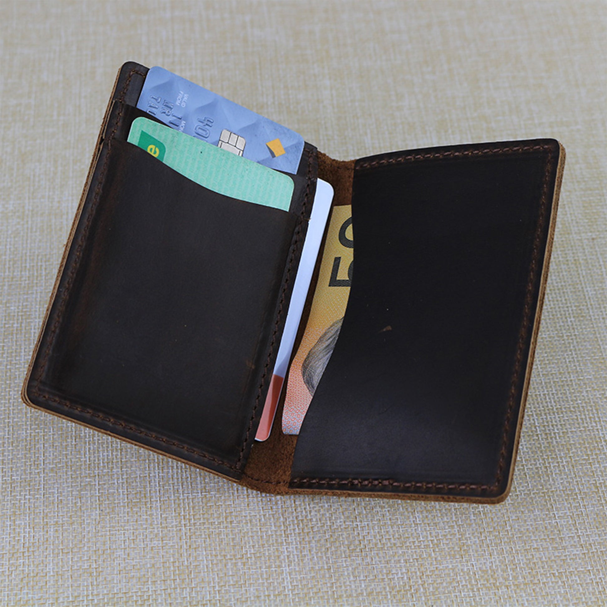 Open trifold custom leather card wallet with cards and money on a textured fabric background