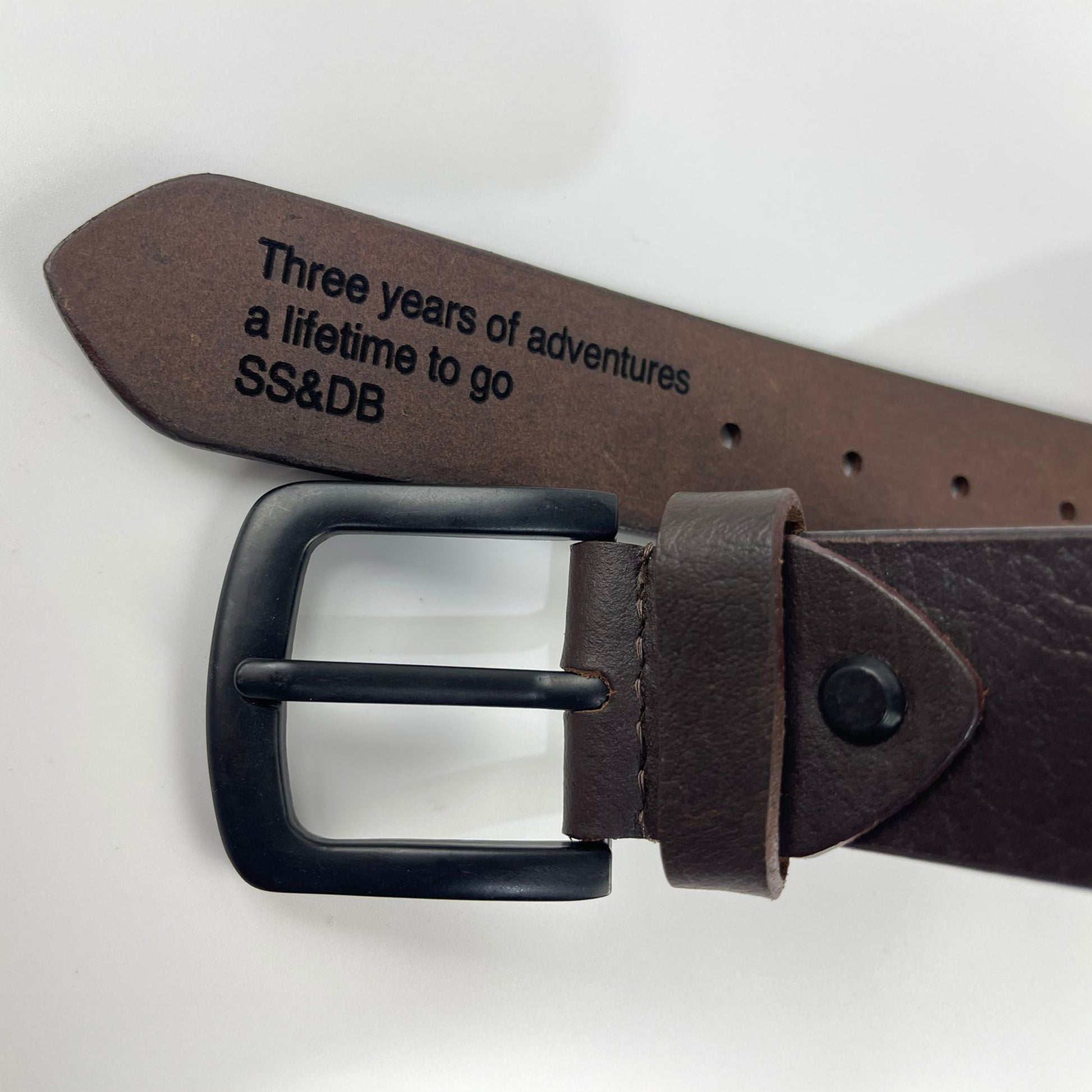 Brown leather belt with engraved message on a light gray background