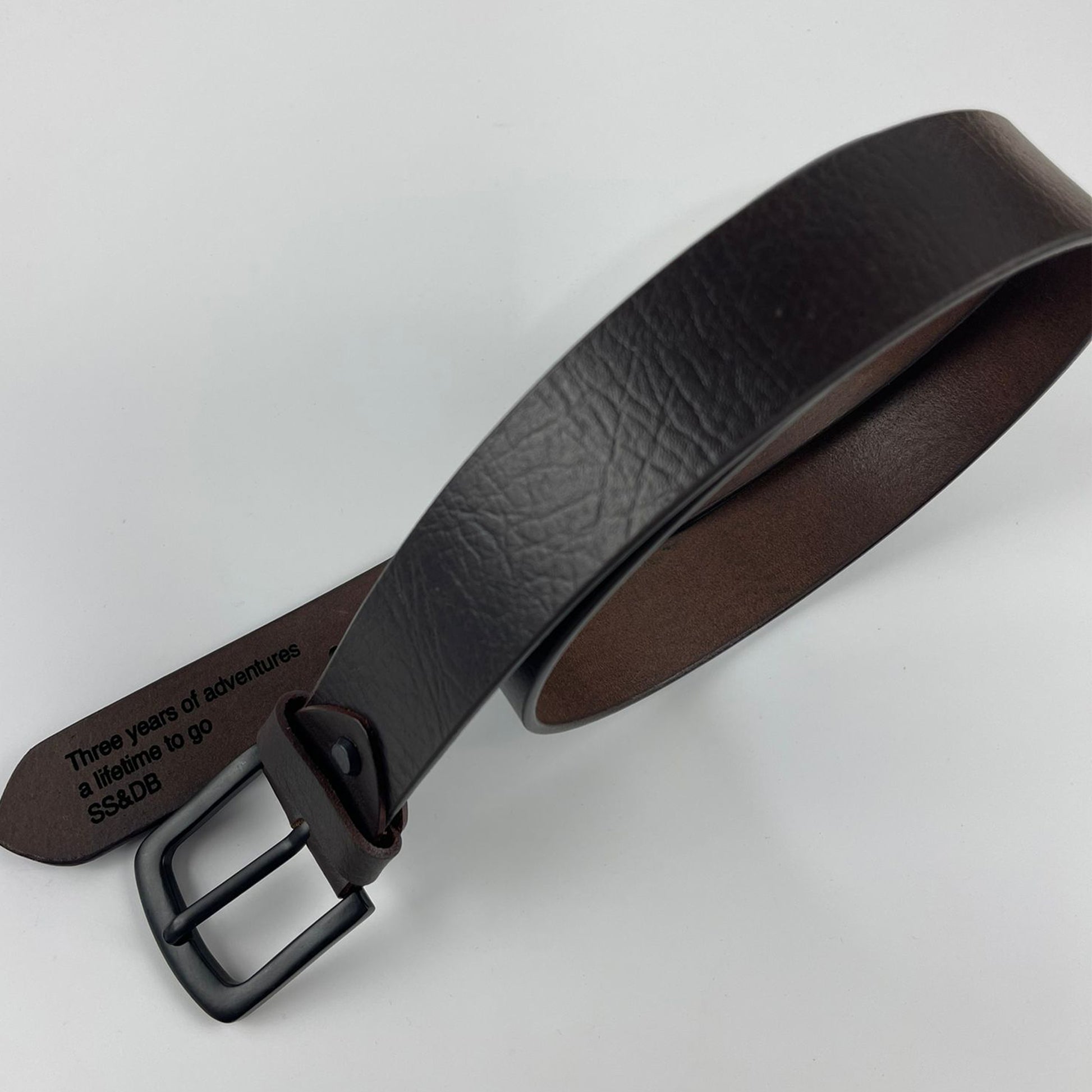 Brown leather belt with black buckle on a light gray background