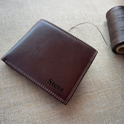 Brown leather wallet with 'Steve' engraving on it placed on a textured beige surface