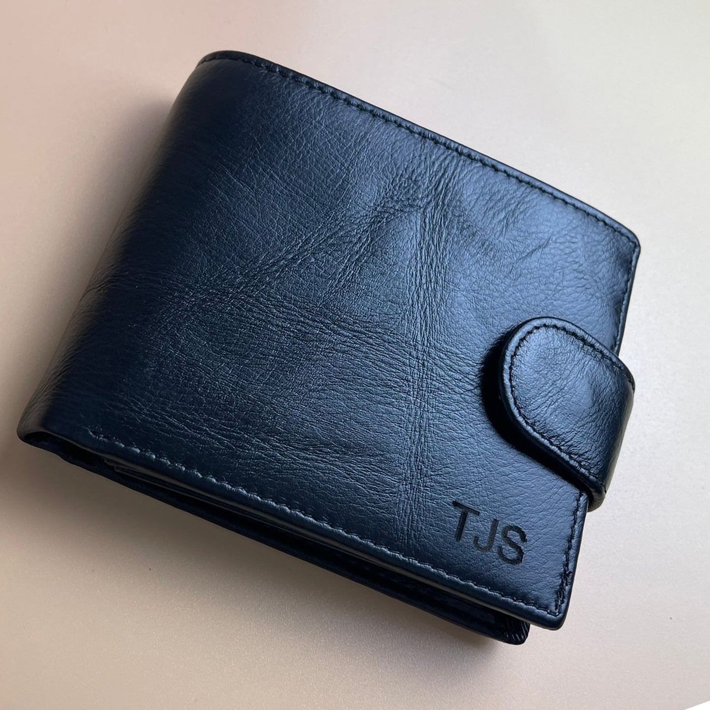 Blue leather wallet with 'TJS' initials on a beige background