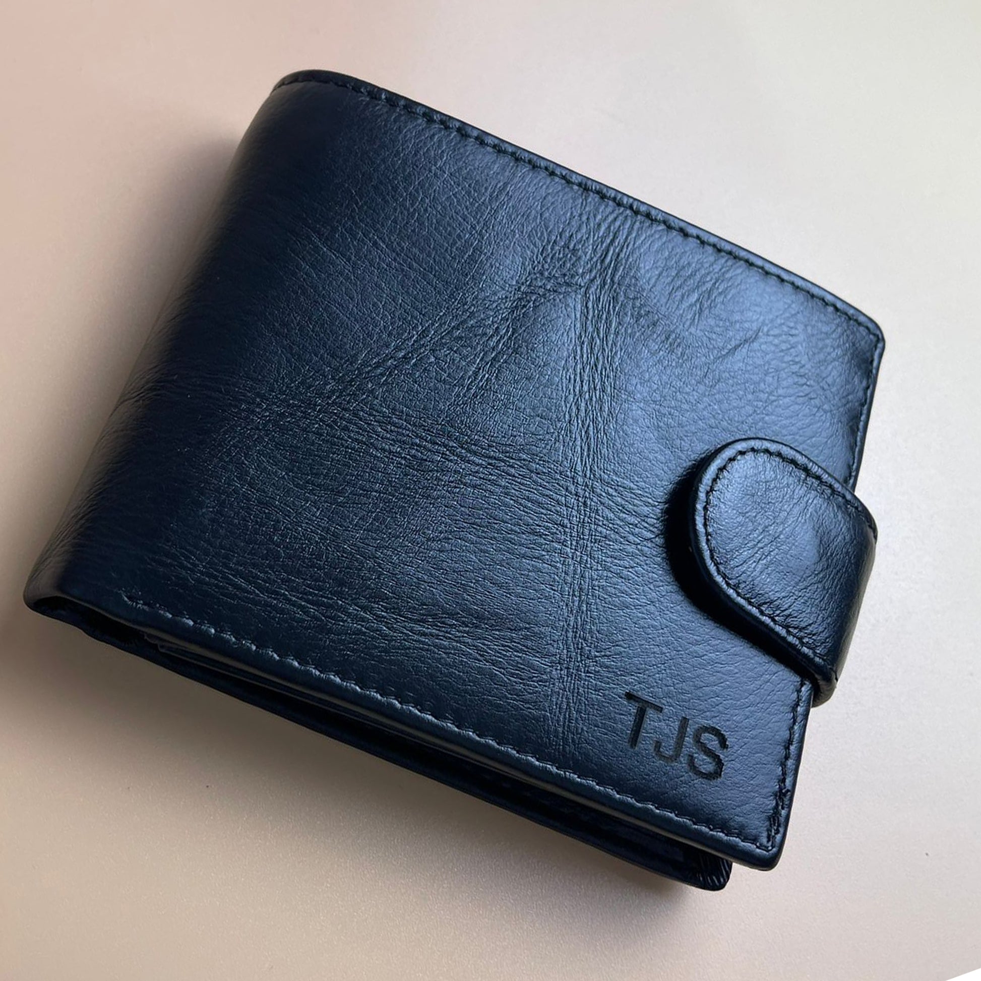 Blue leather wallet with 'TJS' initials on a beige background