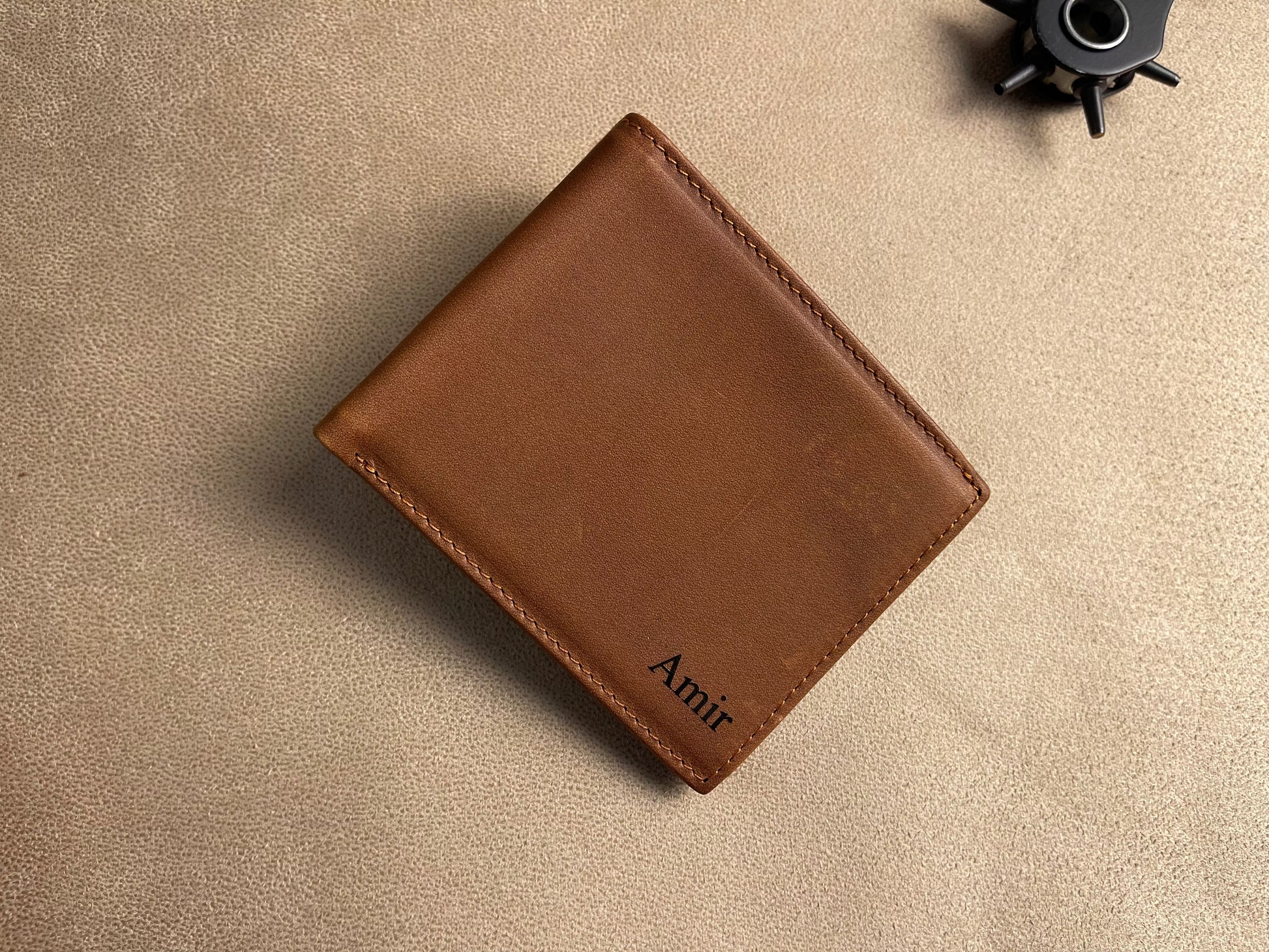 Brown leather wallet with 'Amit' branding on a beige surface