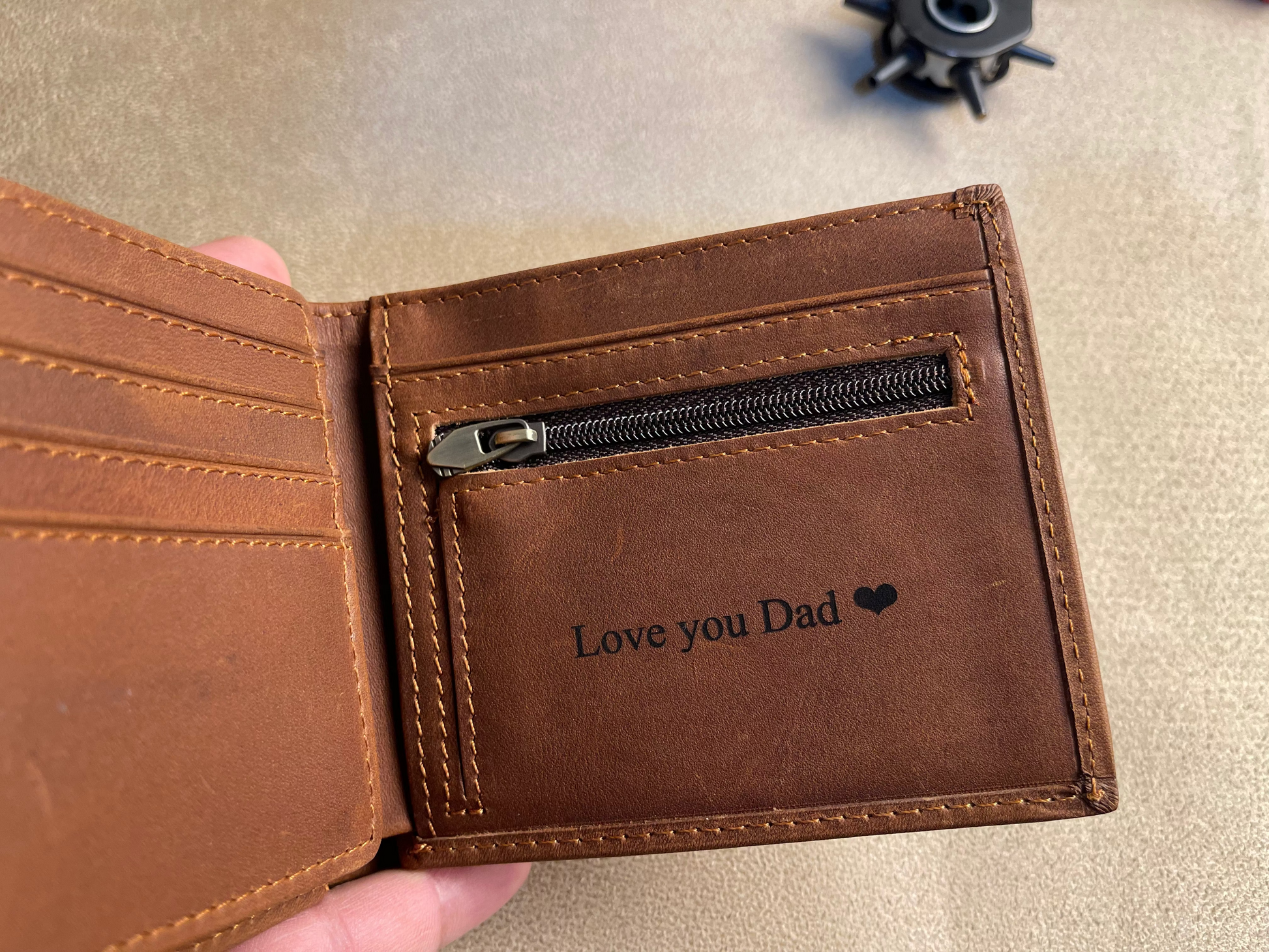 Brown leather wallet with 'Love you Dad' text and black heart symbol on beige surface