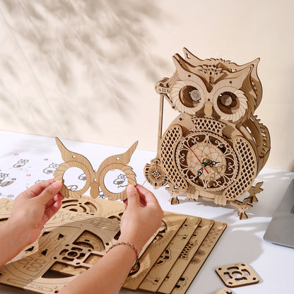 Wooden owl clock kit with hands assembling a wooden owl clock on a light surface.