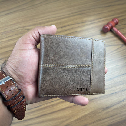 Personalised brown leather wallet with 'MER' initials held by a hand on a wooden surface.