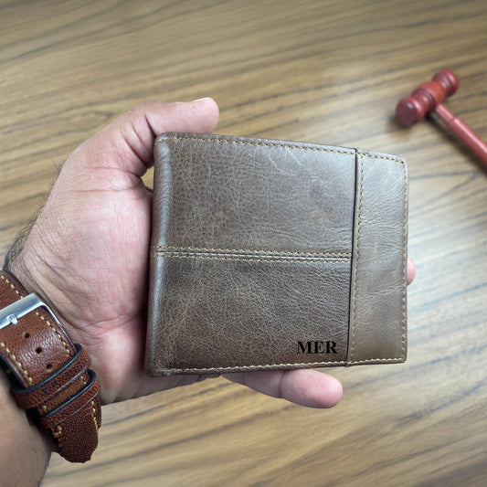 Personalised brown leather wallet with 'MER' initials held by a hand on a wooden surface.