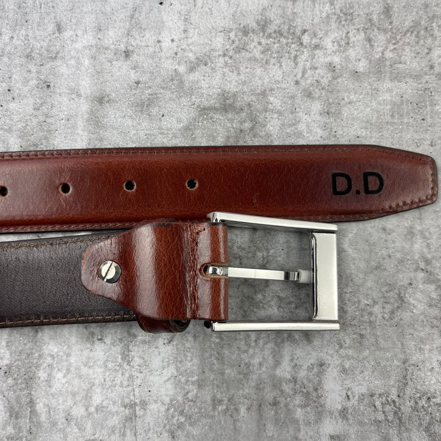 Brown leather belt with silver buckle on a gray surface