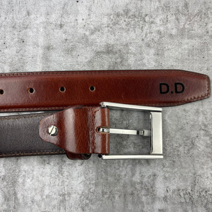 Brown leather belt with silver buckle on a gray surface