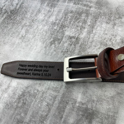 Brown leather belt with engraved message on a gray surface