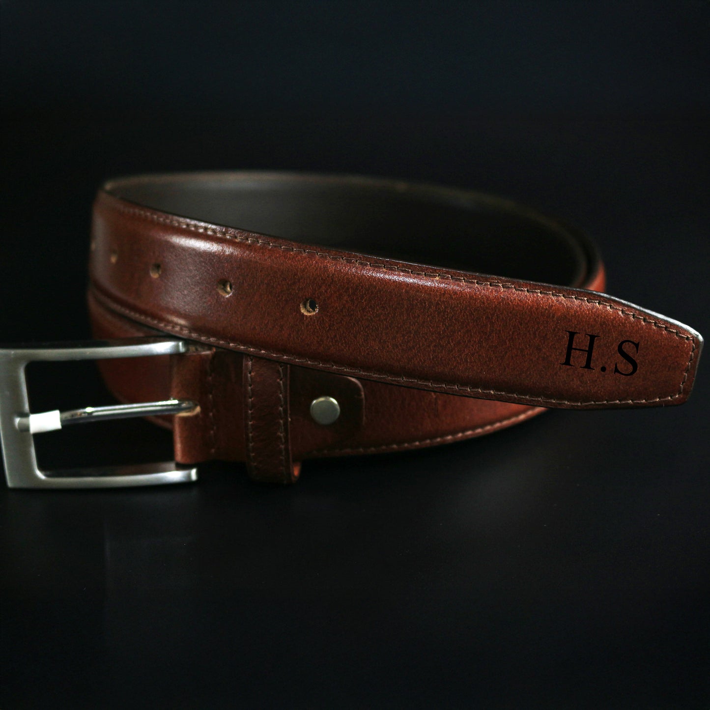 Brown leather belt with silver buckle on a black background