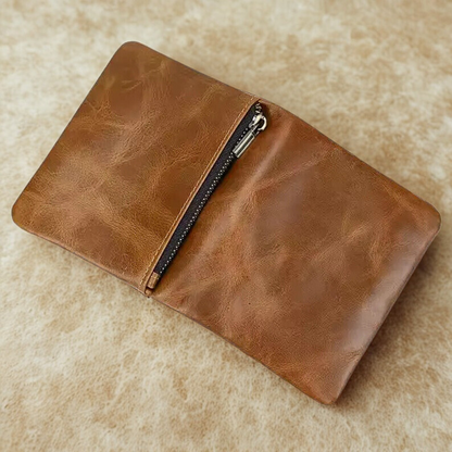 A zipped compartment on the back side of the Brown leather vertical wallet with a zipper on a beige surface