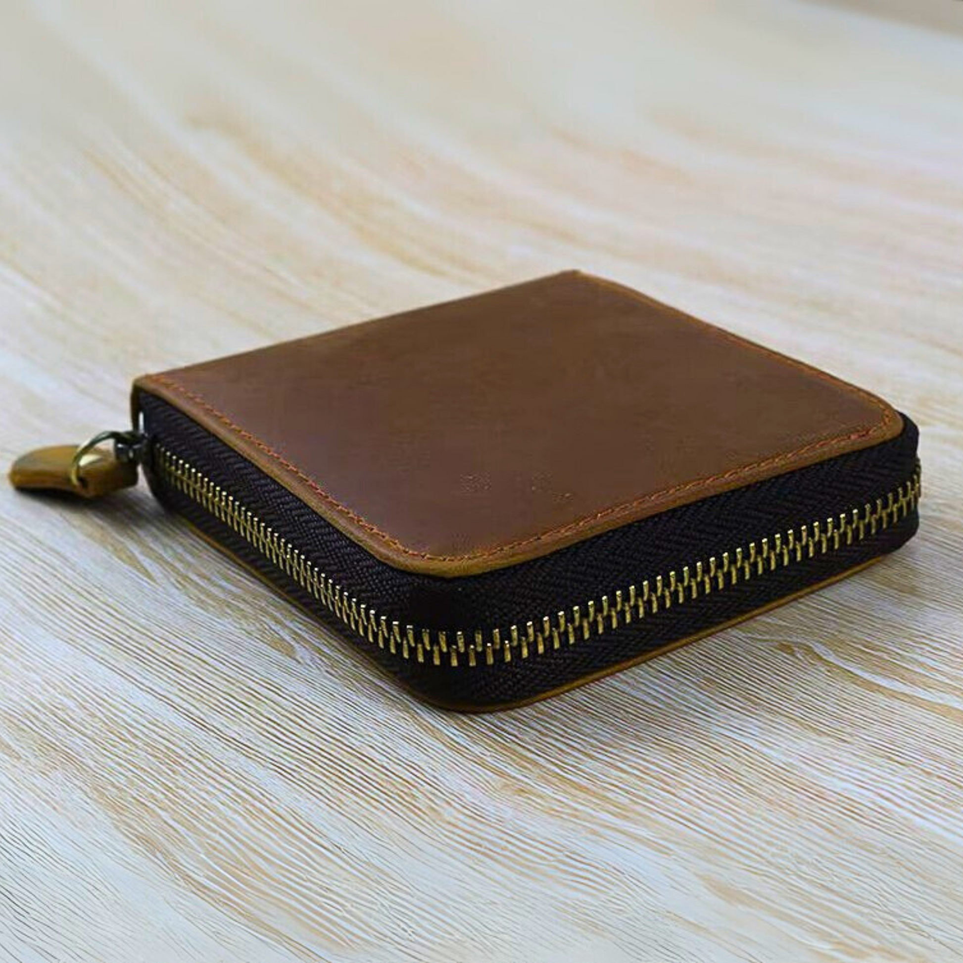 Brown and black zippered leather  wallet on a light wooden surface.