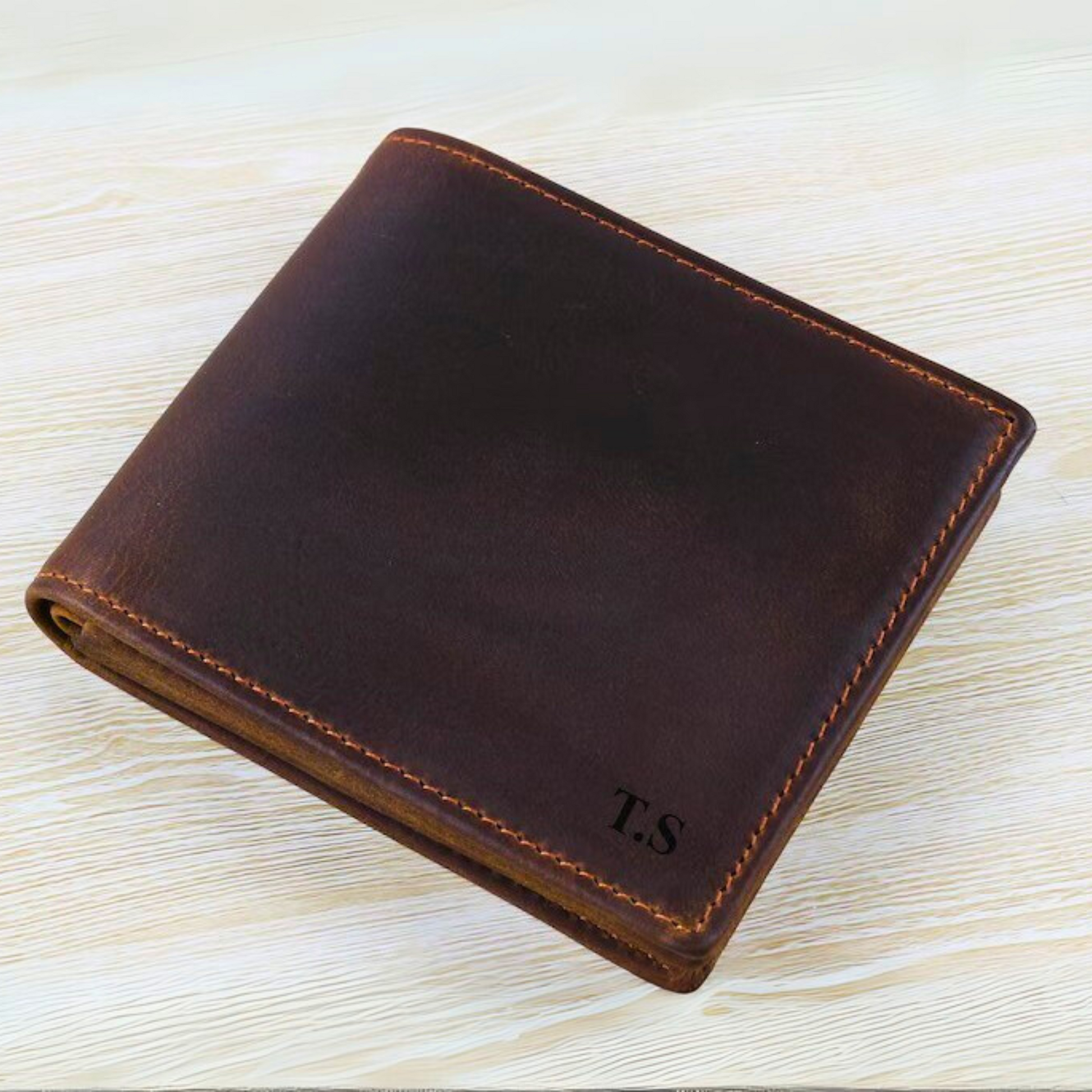 Brown leather wallet with initials 'T.S.' on a light wooden surface
