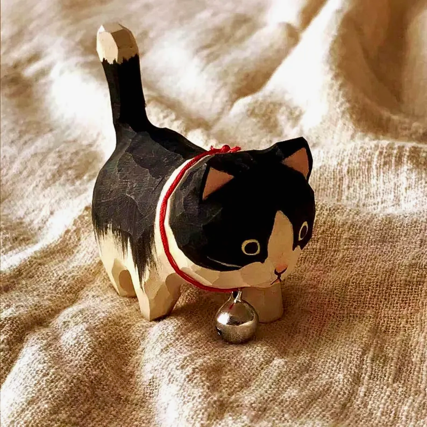 A wooden cat-shaped hand carved figurine with a red collar and bell for housewarming or decorating.