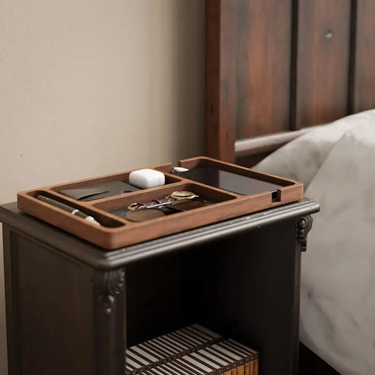 Wooden valet tray with leather lining on nightstand holding watch glasses wallet and airpods next to bed 