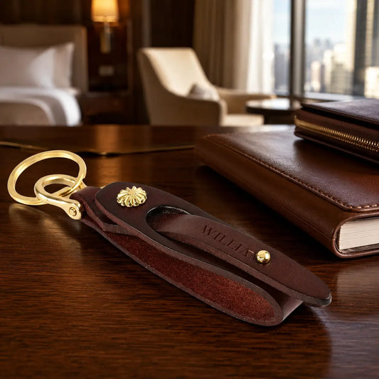 Brown leather key holder with brass key ring and snap fastenings displayed beside leather notebook on wooden desk