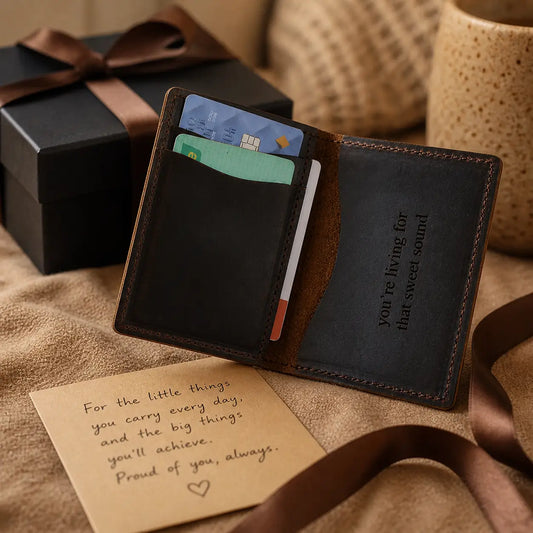 Personalized dark brown leather bi-fold wallet with a custom engraved message, displayed next to a black gift box with a brown ribbon and a sentimental handwritten note.