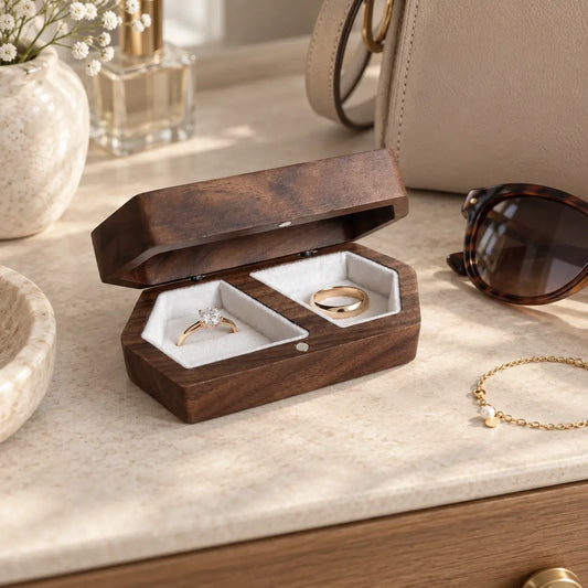 Dark walnut wooden double ring box with two white ring holders displaying engagement and wedding rings on a neutral dressing table.