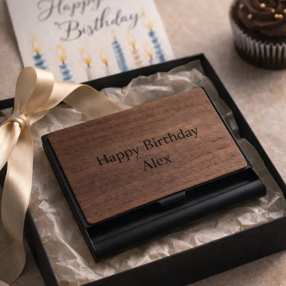 Personalized wooden business card holder engraved with “Happy Birthday Alex” presented inside a luxury black gift box with ribbon, birthday card, and cupcake in a cozy celebration setup.