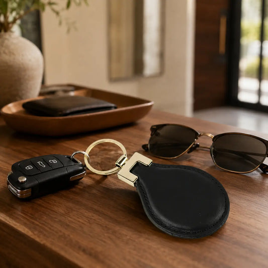 Black leather keychain with gold hardware styled with car keys, sunglasses and wallet on a wooden table