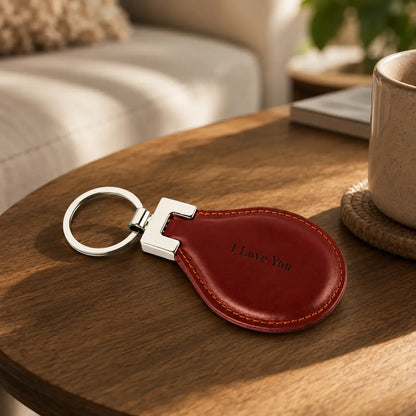 Red-brown personalised leather keychain engraved with I Love You displayed on a wooden table beside a mug
