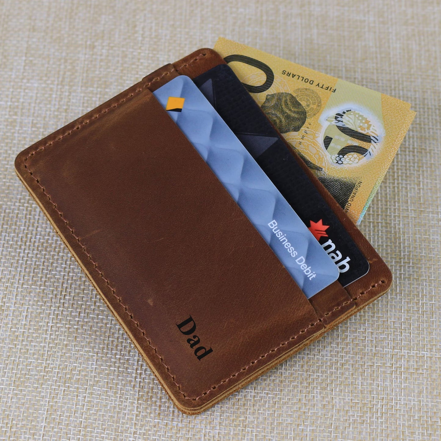 Minimalist tan leather travel cardholder held in an airport setting with an Australian passport, showcasing its compact, front-pocket size.
