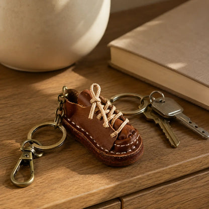 Brown leather shoe keychain displayed with keys and brass hardware on a wooden table