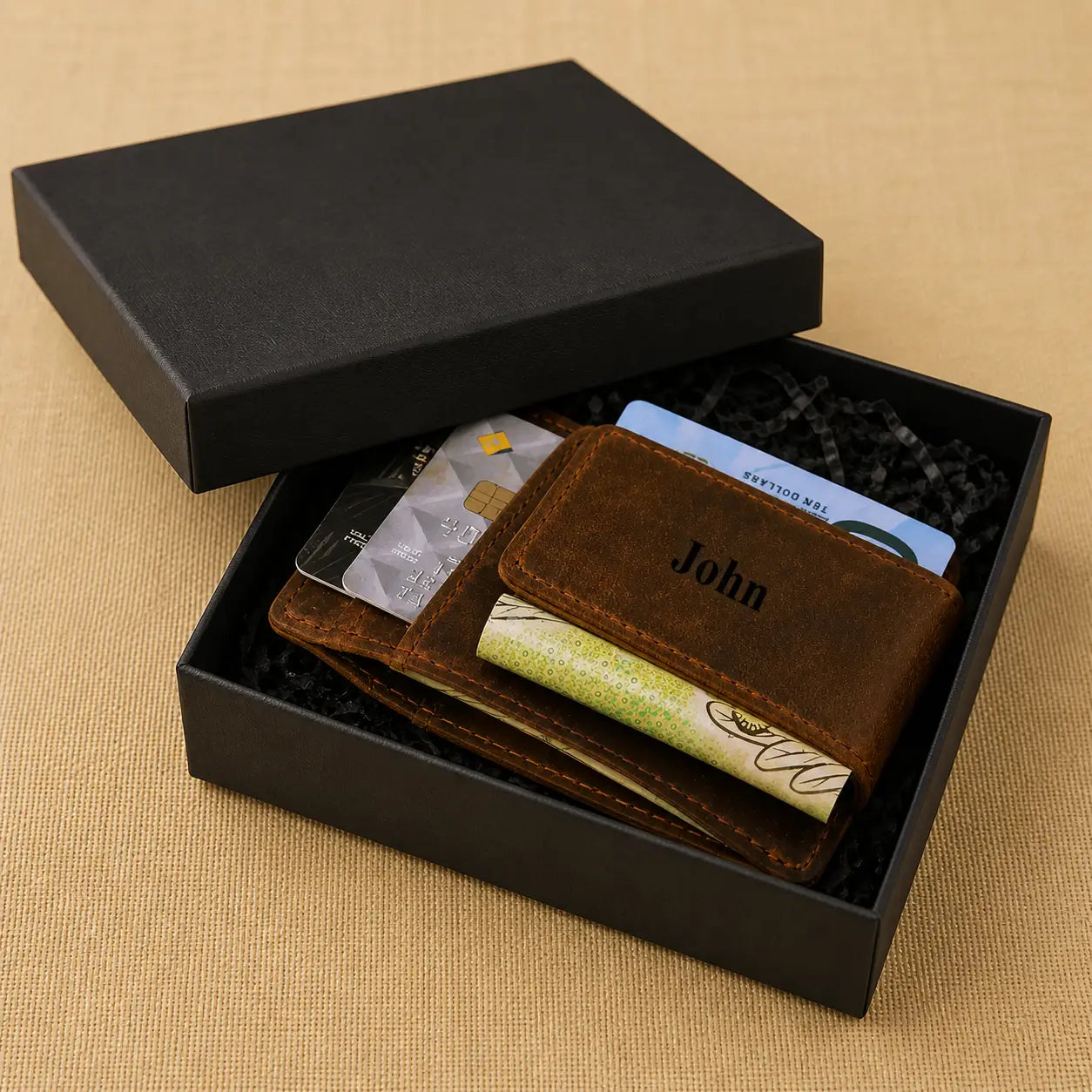 Brown handmade leather card sleeve showing custom personalization, credit cards, and cash, displayed inside its gift packaging on a neutral surface.