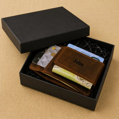 Brown handmade leather card sleeve showing custom personalization, credit cards, and cash, displayed inside its gift packaging on a neutral surface.