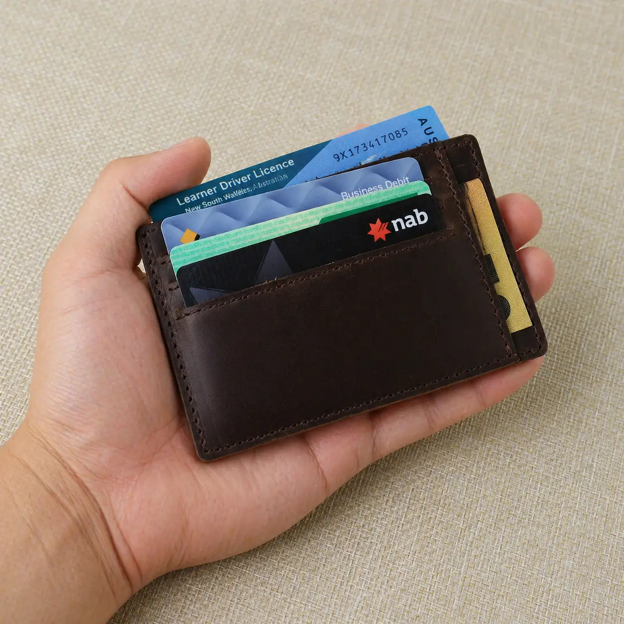 A person holding a dark brown pebbled leather wallet with a personalized name engraving and visible perimeter stitching.